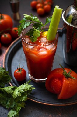 Klasik alkollü Bloody Mary kokteyli. Buzlu, limonlu ve kerevizli. Koyu renkli bir masada kokteyl malzemeleri ve bar araçları.