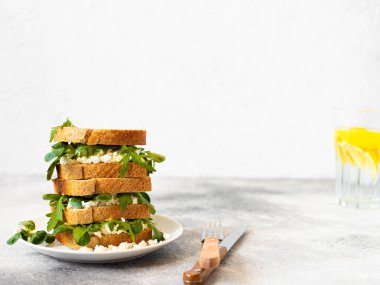 Açık gri bir masa ve beyaz arka planda, ricotta ve roka ile servis edilen sağlıklı bir sandviç. Sağlıklı kahvaltı. Yakın plan. Boşluğu kopyala