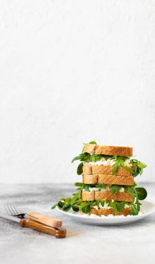 Açık gri bir masa ve beyaz arka planda, ricotta ve roka ile servis edilen sağlıklı bir sandviç. Sağlıklı kahvaltı. Yakın plan. Boşluğu kopyala