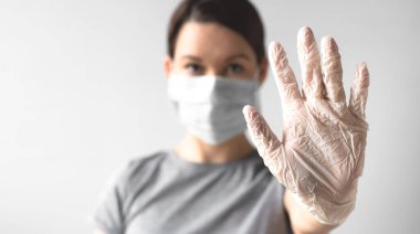 Coronavirus konsepti. Koruyucu tıbbi maske takan bir kız jest duruşu gösteriyor. Tıbbi steril eldiven verin. Sağlığınızı koruyun. Virüsü ve salgını durdurun.