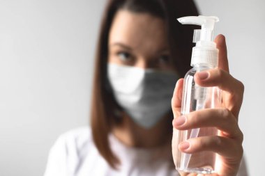Coronavirus konsepti. Koruyucu tıbbi maske takan bir kız elinde dezenfektanla bir şişe tutuyor. Salgın covid-19 virüsünün korunması sırasında hijyen. Sağlığınızı koruyun.