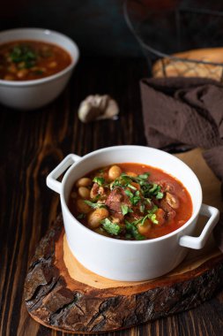 Bean soup with meat and vegetables served on a rustic board and wooden table with bread and garlic. Traditional Balkan soup Pasulj (Grah). Close-up, selective focus clipart
