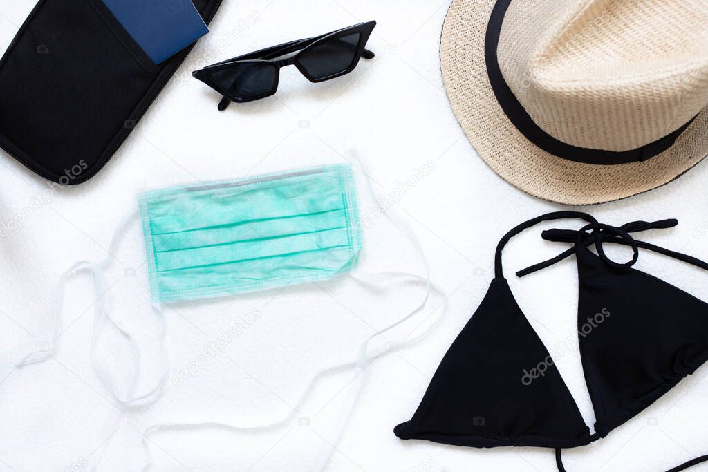 Summer during the coronavirus pandemic. Concept summer 2020 with covid-19. Protective medical mask, swimsuit, passport, sunglasses, straw hat. Flat lay