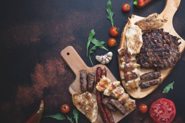 Ahşap kesim tahtalarında çeşitli ızgara etler, taze sebzeler ve koyu kırsal bir zeminde ekmek servis ediliyor. Rostilj adı verilen geleneksel Sırp ve Balkan bbq eti. Düz yatıyordu. Boşluğu kopyala 
