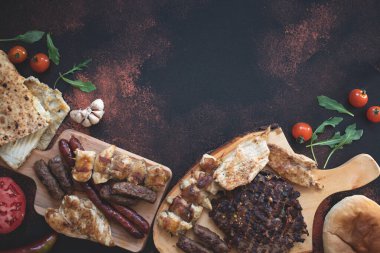 Ahşap kesim tahtalarında çeşitli ızgara etler, taze sebzeler ve koyu kırsal bir zeminde ekmek servis ediliyor. Rostilj adı verilen geleneksel Sırp ve Balkan bbq eti. Düz yatıyordu. Boşluğu kopyala 