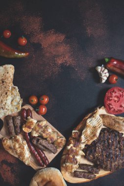 Ahşap kesim tahtalarında çeşitli ızgara etler, taze sebzeler ve koyu kırsal bir zeminde ekmek servis ediliyor. Rostilj adı verilen geleneksel Sırp ve Balkan bbq eti. Düz yatıyordu. Boşluğu kopyala 