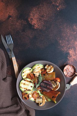 Izgara sebzeler (kabak, kiraz domatesleri, soğanlar, şampiyonlar, dolmalık biberiye ve deniz tuzu ile birlikte koyu renkli bir arka planda servis edilir). Üst Manzara. Boşluğu kopyala