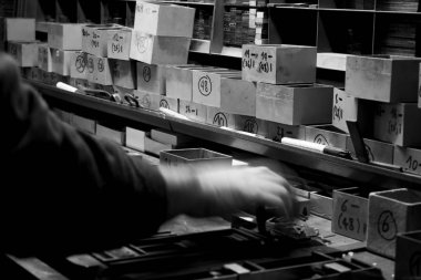 Metalik harfleri ve eski bir tipografinin yazdırma bloklarını düzenleyen elin yakın çekimi, siyah ve beyaz fotoğraf