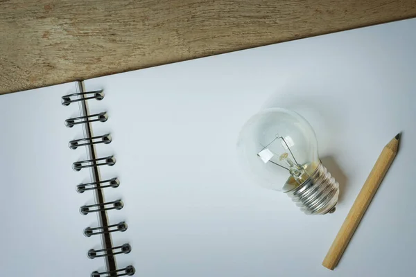 Een gloeilamp met een klein potlood geplaatst op een geopende schetsboek — Stockfoto