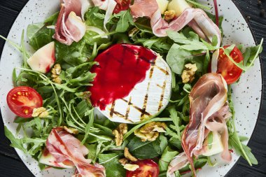 Izgara camembert, roka, ıspanak, jamon, siyah arka planda beyaz domatesli lezzetli salata. Kapat.