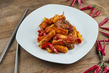 Tteok-bokki - geleneksel Kore mutfağı yemeği, ahşap arka planda domuz pirzolası ve kızarmış pirinç keki. Kapatın. Seçici odak