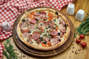 Salamlı, jambonlu, zeytinli, domatesli, peynirli ve tahta tepside beyaz soslu pizza. Tahta bir masanın üzerindeki malzemelerle kompozisyon halinde pizza.