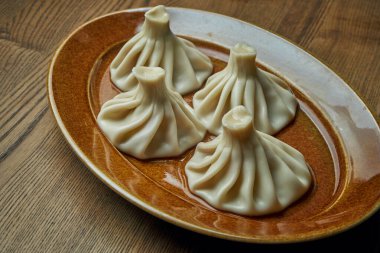 Ahşap bir arka planda kahverengi bir tabakta farklı dolgularla (kıyma, peynir, sebze veya ıspanak) ev yapımı iştah açıcı khinkali. Geleneksel Gürcü mutfağı. Gürcistan hamur tatlısı