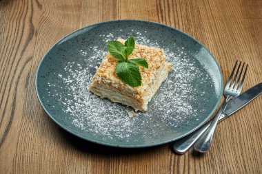 Napolyon 'un kek parçasına yakından bak. Ahşap arka planda seramik tabakta çilek var. Rus mutfağı, kremalı çok katmanlı pasta. Seçici odak