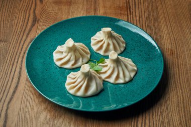 Ahşap bir arka planda mavi bir tabakta farklı dolgularla (kıyma, peynir, sebze veya ıspanak) ev yapımı iştah açıcı khinkali. Geleneksel Gürcü mutfağı. Gürcistan hamur tatlısı