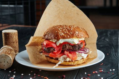 İştah açıcı ve sulu burger köfte, erimiş kırmızı peynir, domates, soğan ve patates kızartması ile birlikte beyaz tabakta lahana. Kapat.