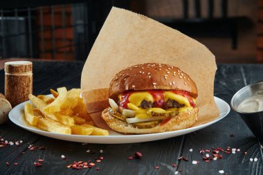İştah açıcı ve sulu burger sığır eti, erimiş çedar peyniri, ketçap, soğan ve salatalık turşusu ile patates kızartması. Kapat.