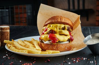 İştah açıcı ve sulu burger sığır eti, erimiş çedar peyniri, ketçap, soğan ve salatalık turşusu ile patates kızartması. Kapat.