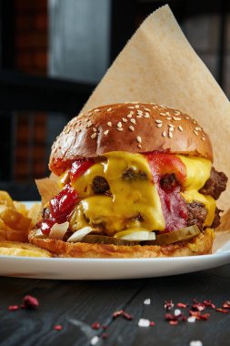 İştah açıcı ve sulu burger sığır eti, erimiş çedar peyniri, ketçap, soğan ve salatalık turşusu ile patates kızartması. Yakın, dikey