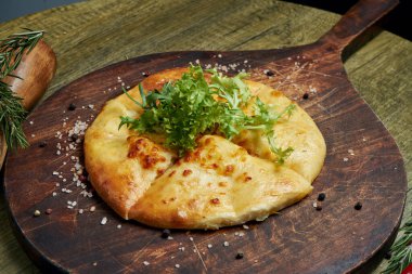 Lezzetli geleneksel Khachapuri 'ye yakından bakın - eritilmiş tuzlu peynirle doldurulmuş kapalı turta (suluguni) ya da ahşap tepside et. Geleneksel Gürcü yemekleri