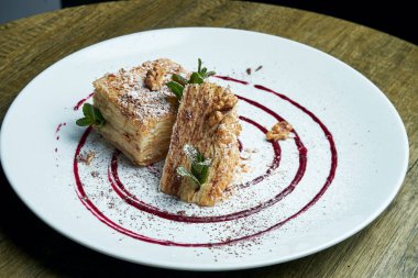 Napolyon 'un kek parçasına yakından bak. Ahşap arka planda seramik tabakta çilek var. Rus mutfağı, kremalı çok katmanlı pasta. Seçici odak