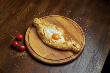 Geleneksel Adjarian Khachapuri 'ye yakın durun - eritilmiş tuzlu peynirli açık turta (suluguni) ve ahşap tepside yumurta sarısı. Geleneksel Gürcü yemekleri