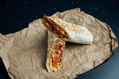 Et, salata ve ev yapımı sos ile nefis shawarma dürümü. Siyah arka plandaki el işi kağıdında ince pide ekmeği. Doğu mutfağı. Izgara etle dilimlenmiş kebap..