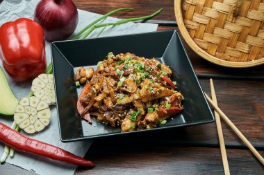 Bebek mısırlı selofan eriştesi, dolmalık biber, soğan, havuç ve tavuklu kızarmış teriyaki soslu ahşap arka planda. Lezzetli Asya sokak yemekleri
