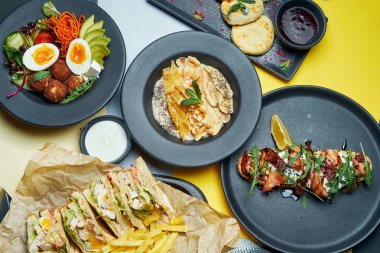 Renkli arka planda farklı yemekler. Falafelli yemek masası, somonlu avokado tostu, peynirli kek, sandviçler ve meyveli yulaf ezmesi. Üst manzara, yemek düzlüğü