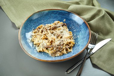 Klasik mantarlı makarna, krema sosu ve ahşap arka planda mavi bir tabakta parmesan. İtalyan ev yapımı mutfak..