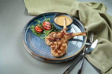 Ahşap bir arka planda mavi bir tabakta fıstık sosu ve kiraz domatesli ızgara buzağı veya kuzu eti. Restoran yemekleri bölüyor.