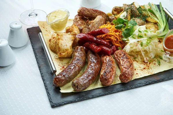 Large dish with grilled sausages, smoked sausages, chicken and pork kebabs with side dishes of baked potatoes and cabbage. Close up, selective focus. White background