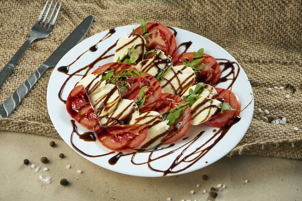 新鮮なトマト 柔らかいモッツァレラチーズ アルグラ ソースとイタリアのカプレーゼサラダを素朴な背景に白いプレート上で食欲をそそるビューを閉じます 健康食品 — ストック写真