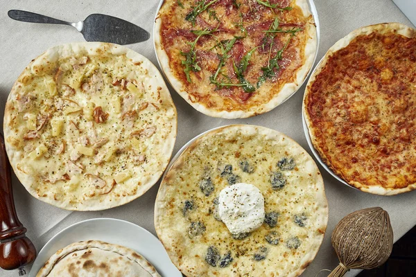 Many different pizzas on a linen tablecloth - margarita pizza, 4 cheeses, with jamon and Hawaiian. Italian dining table. Top view flat lay food.