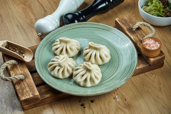 Traditional Georgian dish - khinkali with minced meat or cheese on a blue ceramic plate on a wooden tray. Food flat lay. Georgian dumplings