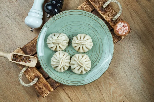 Traditional Georgian dish - khinkali with minced meat or cheese on a blue ceramic plate on a wooden tray. Food flat lay. Georgian dumplings