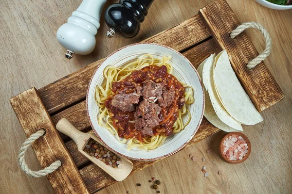 Mexican style noodles - corn paste with chili con carne, stewed beef and tacos in a ceramic plate. Modern mexican cuisine. Food flat lay