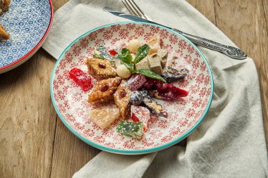 Klasik oryantal tatlılar - ballı ve fındıklı baklava, Türk lokumu, ahşap zemin üzerinde kırmızı seramik bir tabakta kilise kilisesi.