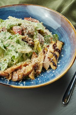 Kıtır ekmekli Sezar salatası, parmesan peyniri, tavuk, ahşap arka planda mavi kasede yumurta. Restoran servisi. Yakın çekim, seçici odaklanma, dikey