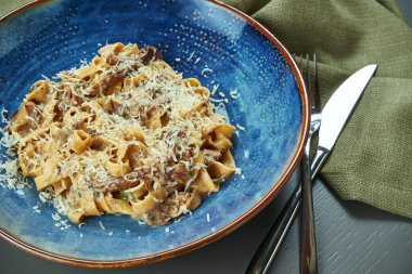 Klasik mantarlı makarna, krema sosu ve ahşap arka planda mavi bir tabakta parmesan. Üst görünüm, düz görünüm, kopyalama alanı