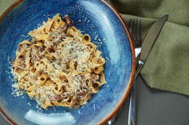 Klasik mantarlı makarna, krema sosu ve ahşap arka planda mavi bir tabakta parmesan. Üst görünüm, düz görünüm, kopyalama alanı