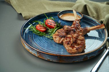 Ahşap bir arka planda mavi bir tabakta fıstık sosu ve kiraz domatesli ızgara buzağı veya kuzu eti. Seçici odak, kapat, boşluğu kopyala