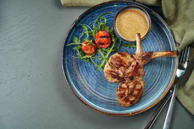 Ahşap bir arka planda mavi bir tabakta fıstık sosu ve kiraz domatesli ızgara buzağı veya kuzu eti. Üst ivew, düz yatar