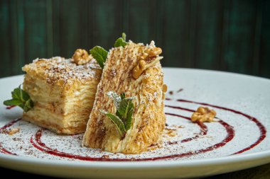 Napolyon 'un kek parçasına yakından bak. Ahşap arka planda seramik tabakta çilek var. Rus mutfağı, kremalı çok katmanlı pasta. Seçici odak