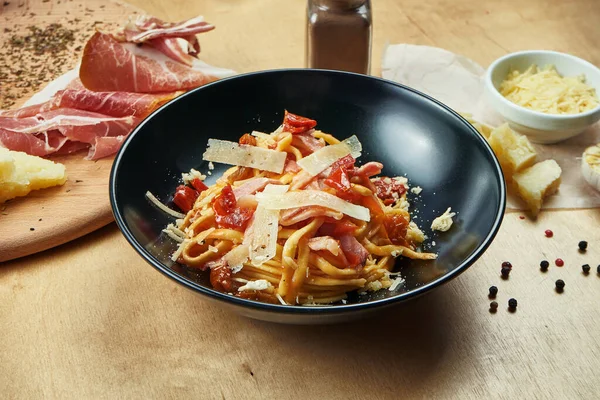 Classic, homemade pasta with red sauce, parmesan, ham and sun-dried tomatoes in black bowl. Traditional italian cuisine