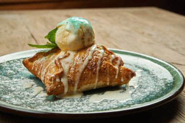 Elmalı turta, ahşap arka planda mavi bir tabakta vanilyalı dondurma. Popüler Avusturya hamur işleri ve tatlı. Kapat.
