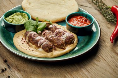 İştah açıcı rulo Lyulya kebabı. Kuzu kıyması üzerine pide ve seramik tabakta salsa sosuyla birlikte kıyma. Dikey, ahşap arka plan, Doğu mutfağı