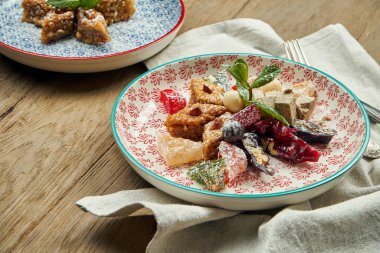 Ahşap zemin üzerinde seramik bir tabakta şam fıstığı ve bal bulunan klasik Türk baklavası. Türk hamur işleri ve tatlıları. Kapat.