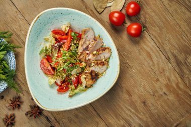 Izgara hindi, domates, fıstık ve ahşap arka planda mavi bir kasede salata. Sağlıklı beslenme