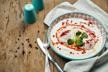 Sağlıklı kahvaltı. Ahşap arka planda mavi bir kasede yoğurt soslu haşlanmış yumurta. Cilbir.